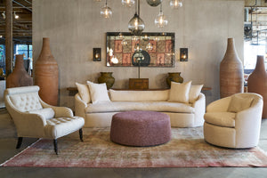  The Grace Chair in a light colored fabric sitting with the Grace Sofa and Juliet chair. There is a maroon ottoman and a vintage rug. In the background, there at tall clay pots and a large mirror on the wall. Photographed in Segura Natural. 