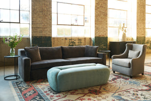  Sofa in a showroom with a turquoise bench and chair on the right. Photographed in Velluto Slate. 
