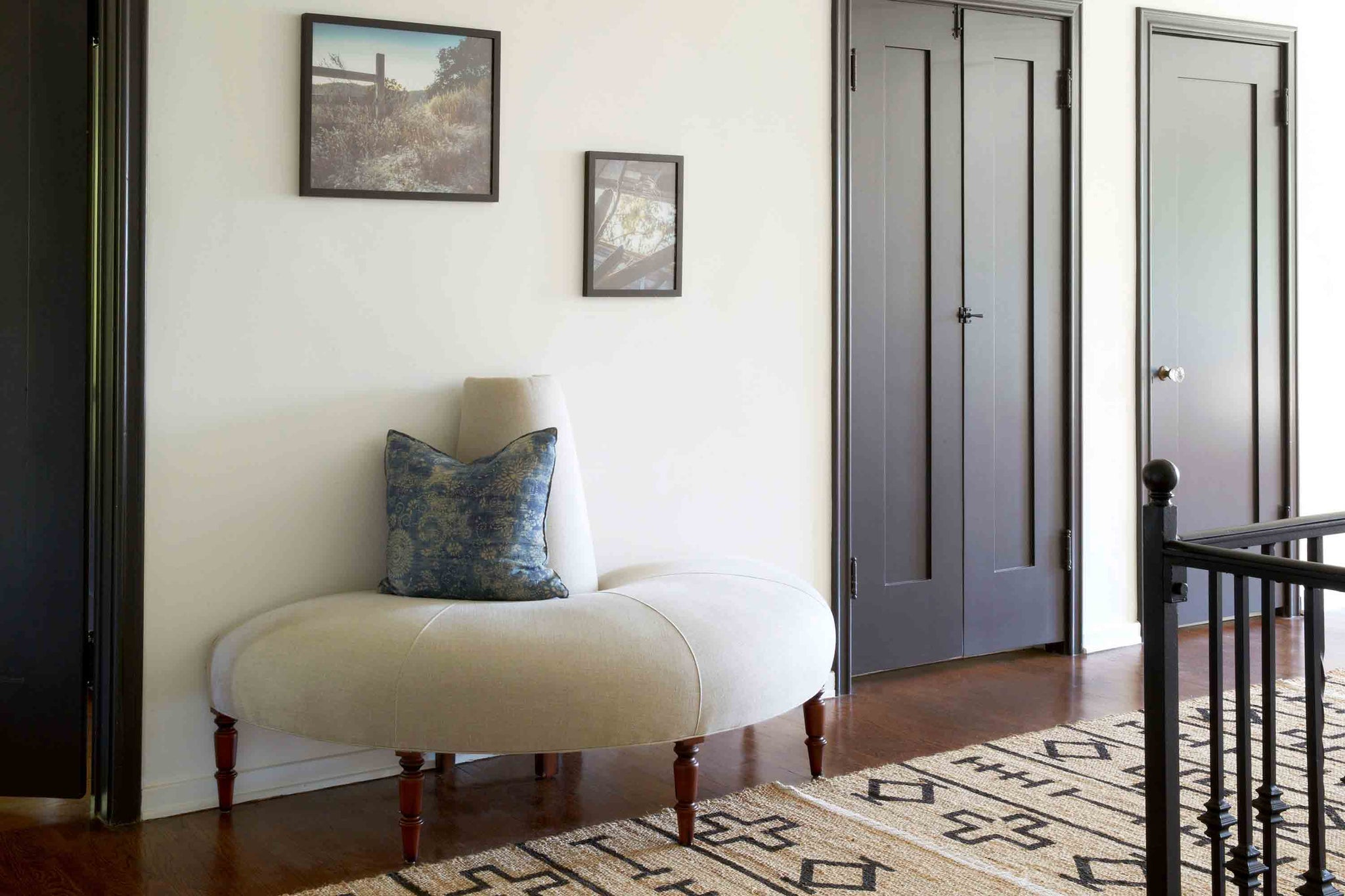  The Half Coin sofa is shown in Vintage Flax linen, a light colored fabric. It is in a hallway, against the wall, between 2 dark doors. There is a blue pillow on it and 2 frames are hanging on the wall. Photographed in Vintage Flax. 