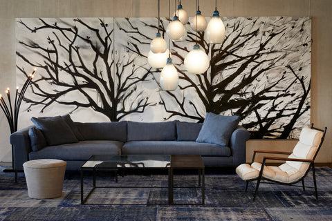 Henrietta 2pc Sectional in Rye Midnight Blue next to a glass coffee table, a light ottoman and a light colored chair. Underneath the pieces os a patterned blue rug. Behind the sectional is a large painting of tree branches. Above hangs multiple jug lamps. Photographed in Rye Midnight.