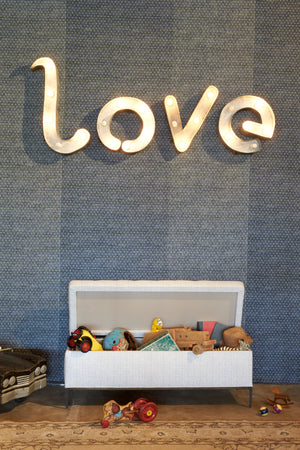  Jaxon chest in Lola Sky Blue. The chest is open with lots of toys within. In the background is a patterned blue wall with vintage letter lights that spell "love."Lola Sky Blue Photographed in Lola Sky Blue 