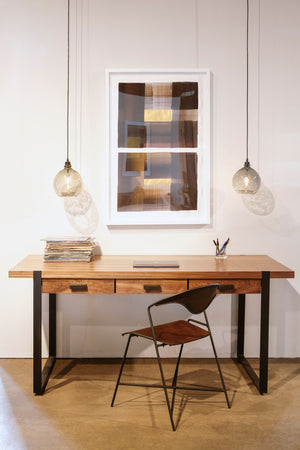  Wood desk with metal base against white wall with at work and two small jug lamps hanging on either side in smoke finish. 