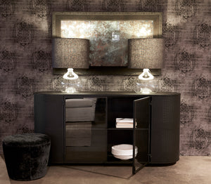  Isaac oval credenza with two jug oval table lamps in clear finish with dark grey lamp shades. Polly ottoman in dark velvet fabric. Fabric upholster back wall in dark print and mirror hung up.  