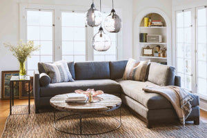  Living room with upholstered sectional in grey fabric, round wood coffee table with metal base placed in front of the sectional. Above the the coffee table is three jug lamps extra large in smoke finish. 