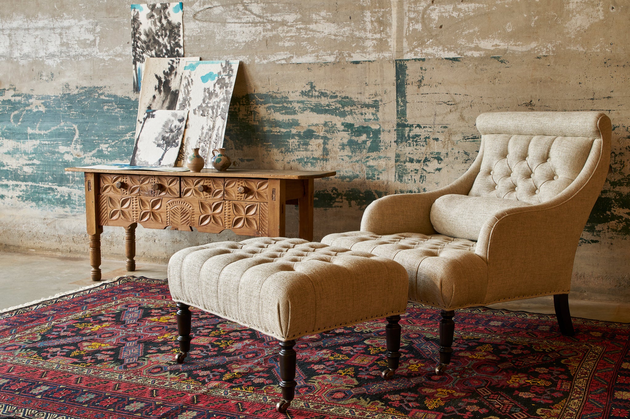  The Juliet chair and ottoman are angled in front of a concrete wall and next to a carved wood credenza with art on top. Photographed in Avery Oatmeal 
