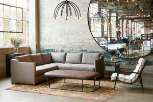  Kardell Sectional in Brevard Pewter next a light ottoman and a light chair. A brown rug sits underneath the the sectional. Above the sectional hangs a chandelier. Photographed in Brevard Pewter. 