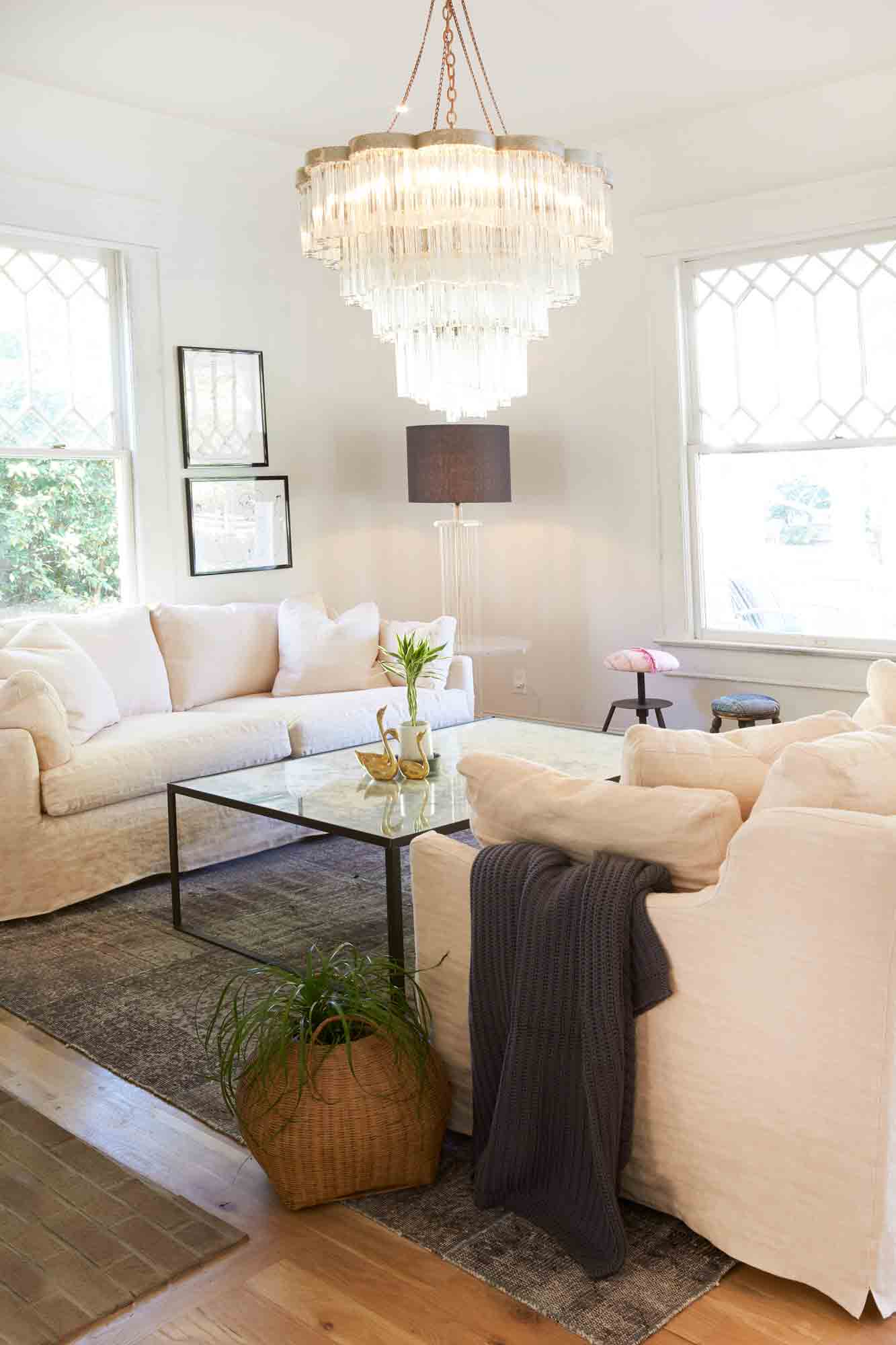  Small living with daylight and two facing Lanister sofas in Brevard Rose linen. A large glass chandelier is hanging above a mirror coffee table. A basket with a plant in it is on the floor and a grey throw is hanging on the armrest. Photographed in Brevard Rose. 