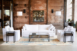  Lanister chairs in Otis White next to a sofa and a coffee table. In the background is a wood wall with a mirror and two lighting lamps. Photographed in Otis White. 