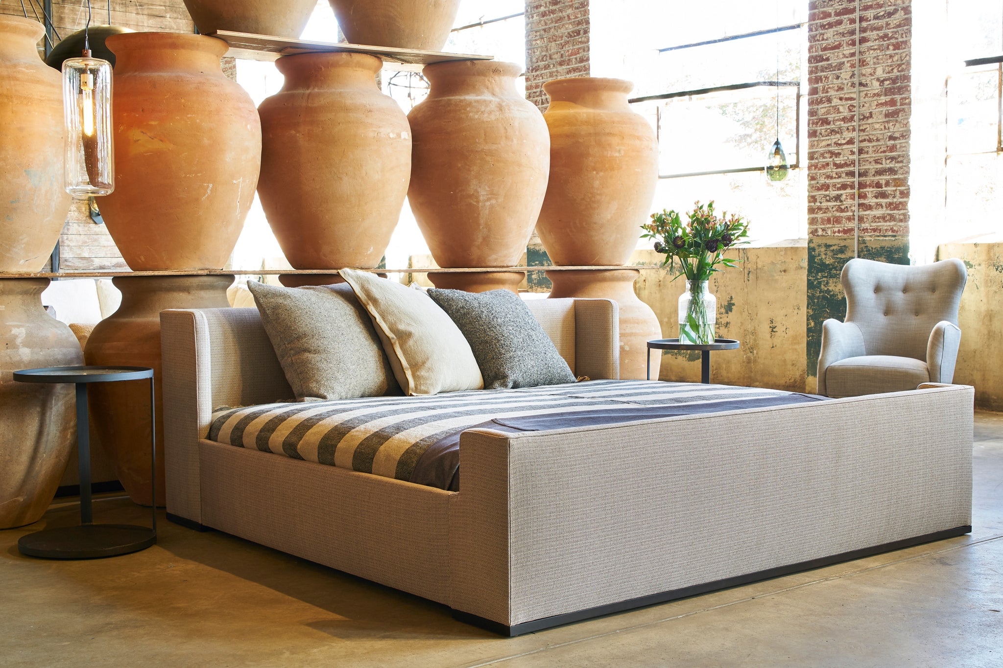  The Laurel Bed is in front of a wall of large clay pots with a Romi Mini Chair next to it. Photographed in Carta Hazelnut. 