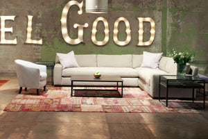  Loft 2 arm Sectional in Naoki Hemp (discontinued) next to a metal coffee table, a light colored chair and glass side table. Underneath the sectional is a red patterned rug. In the background are light up letters that spell Feel Good. Photographed in Naomi Hemp. 
