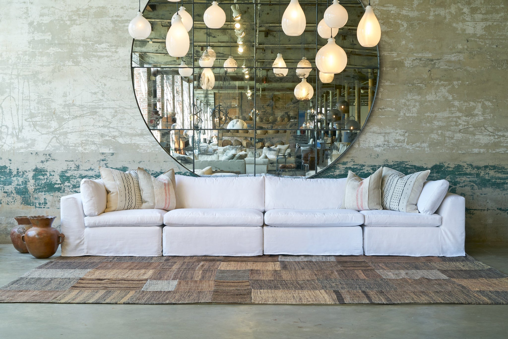  Large white slipcovered modular sofa in front of a large round mirror with white glass lighting pendants. Photographed in Otis White 