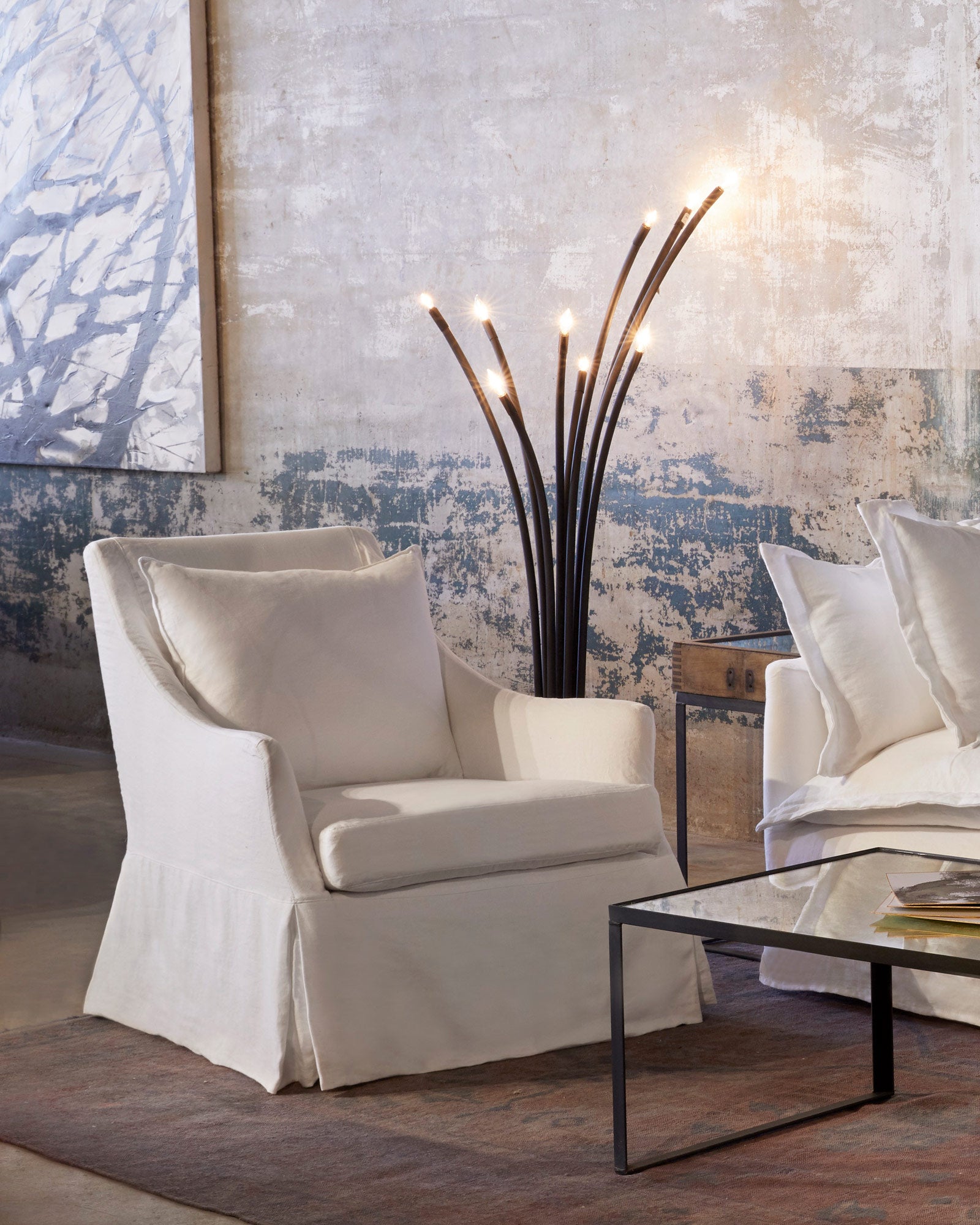  Lucy chair in Otis White next to a metal floor lamp. In the background is a concrete wall with a painting hanging  