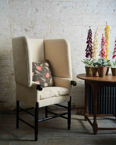  Mantis chair in Velluto Natural next to a wood table with flowers above. In the background is a concrete wall. Photographed in Velluto Natural.