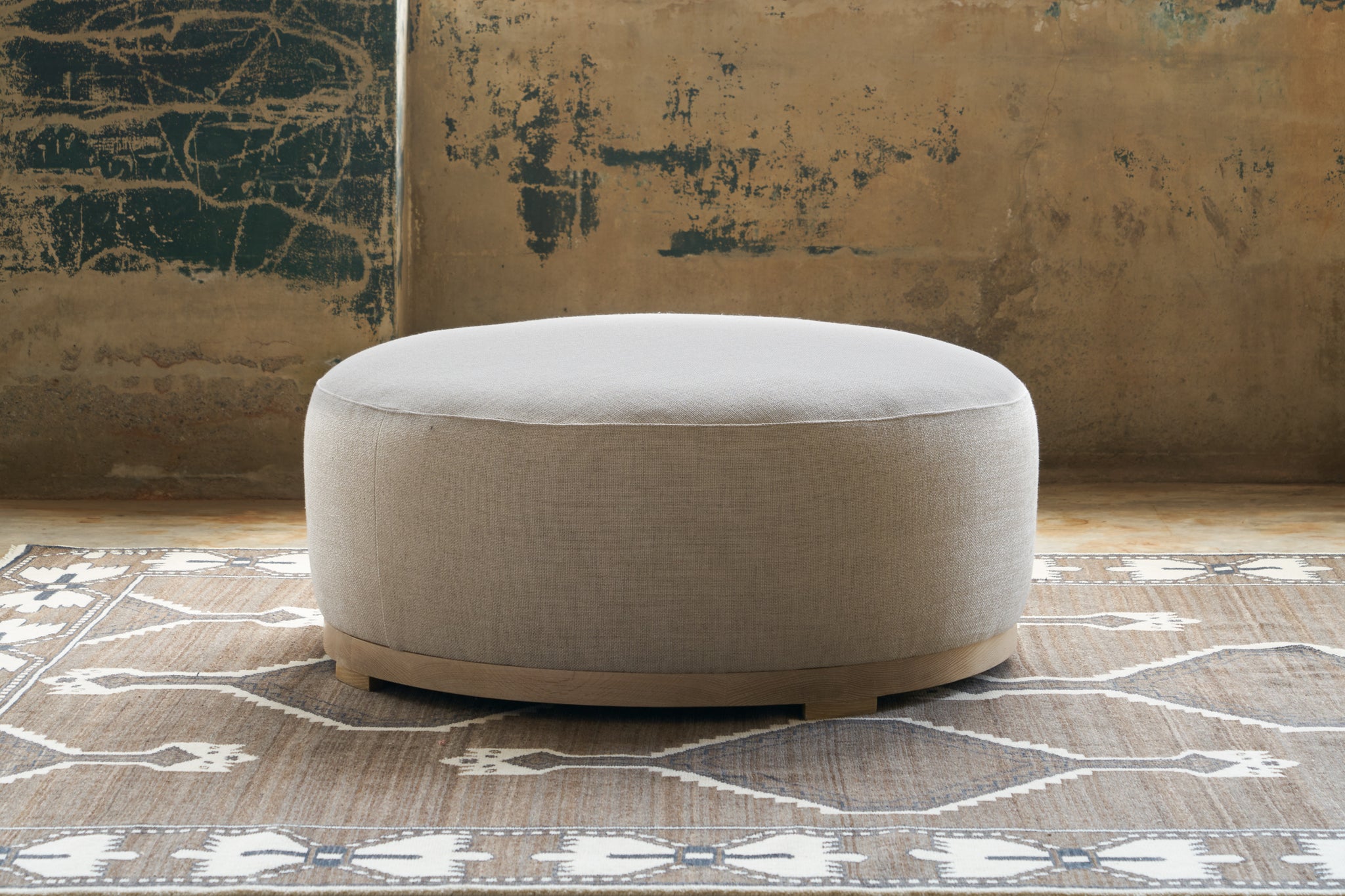  Marco Ottoman in Bellamy Natural on top of a textured rug. Photographed in Bellamy Natural. 
