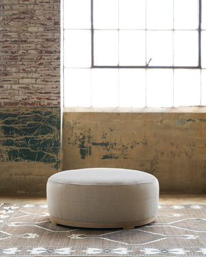 Marco Ottoman in Bellamy Natural on top if a textured rug. Photographed in Bellamy Natural. 