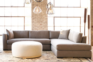  Marco Ottoman in Bellamy Natural next to a grey sectional. Photographed in Bellamy Natural. 