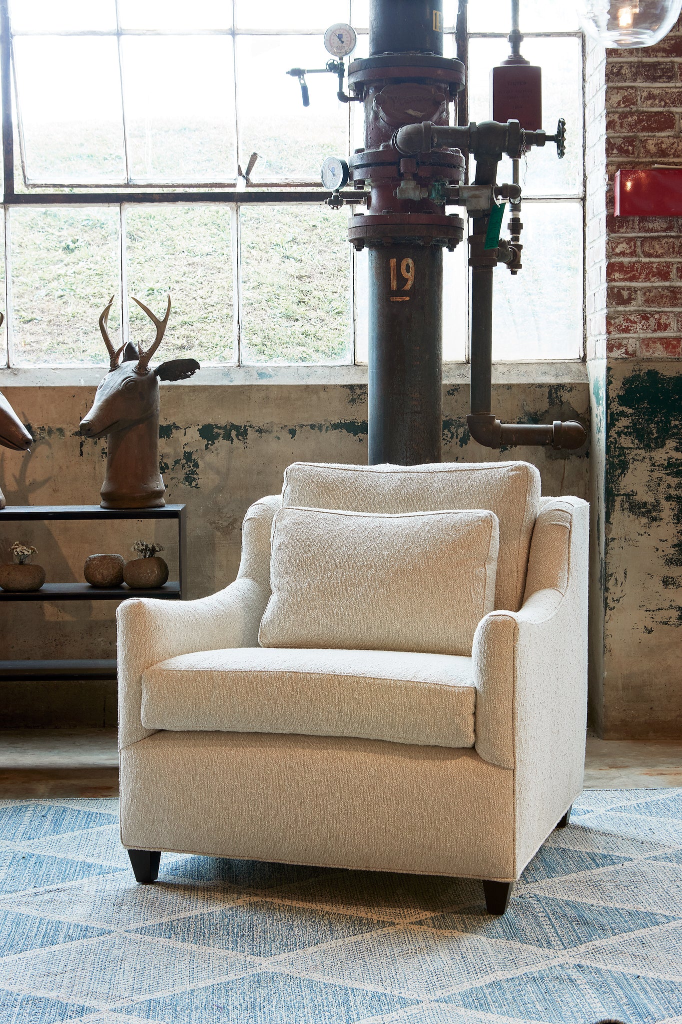  Milo chair in Segura Natural next to a dark credenza with a decorative deer on top. In the background is a brick wall with an industrial pipe. Photographed in Segura Natural. 