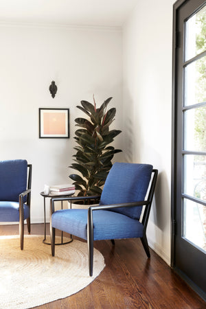  Montauk chair in Blue Alta Dena next to a metal side table and potted plant. In the background is a white wall. Photographed in Blue Alta Dena. 