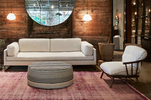  Cream sofa against a wood wall with a wood frame chair on the right and a round stripped ottoman in the middle. Photographed in Rayas Fino. 