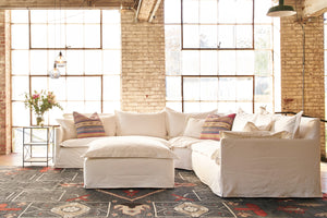  Paloma 2 Arm Sectional in Luna White next to a large ottoman and large windows in the background. Photographed in Luna White. 