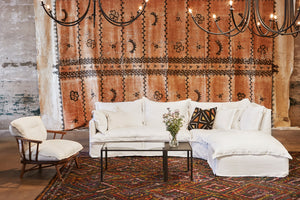  Paloma 3pc Sectional in Otis White next to a white chair and glass coffee table. Underneath the sectional is a multi-colored patterned rug. Above the sectional are multiple chandeliers. Photographed in Otis White. 