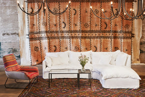  Paloma 3pc Sectional in Otis White next to a red patterned chair and a glass coffee table. Underneath the sectional is a multi-colored patterned rug. Above the sectional are multiple chandeliers. Photographed in Otis White. 