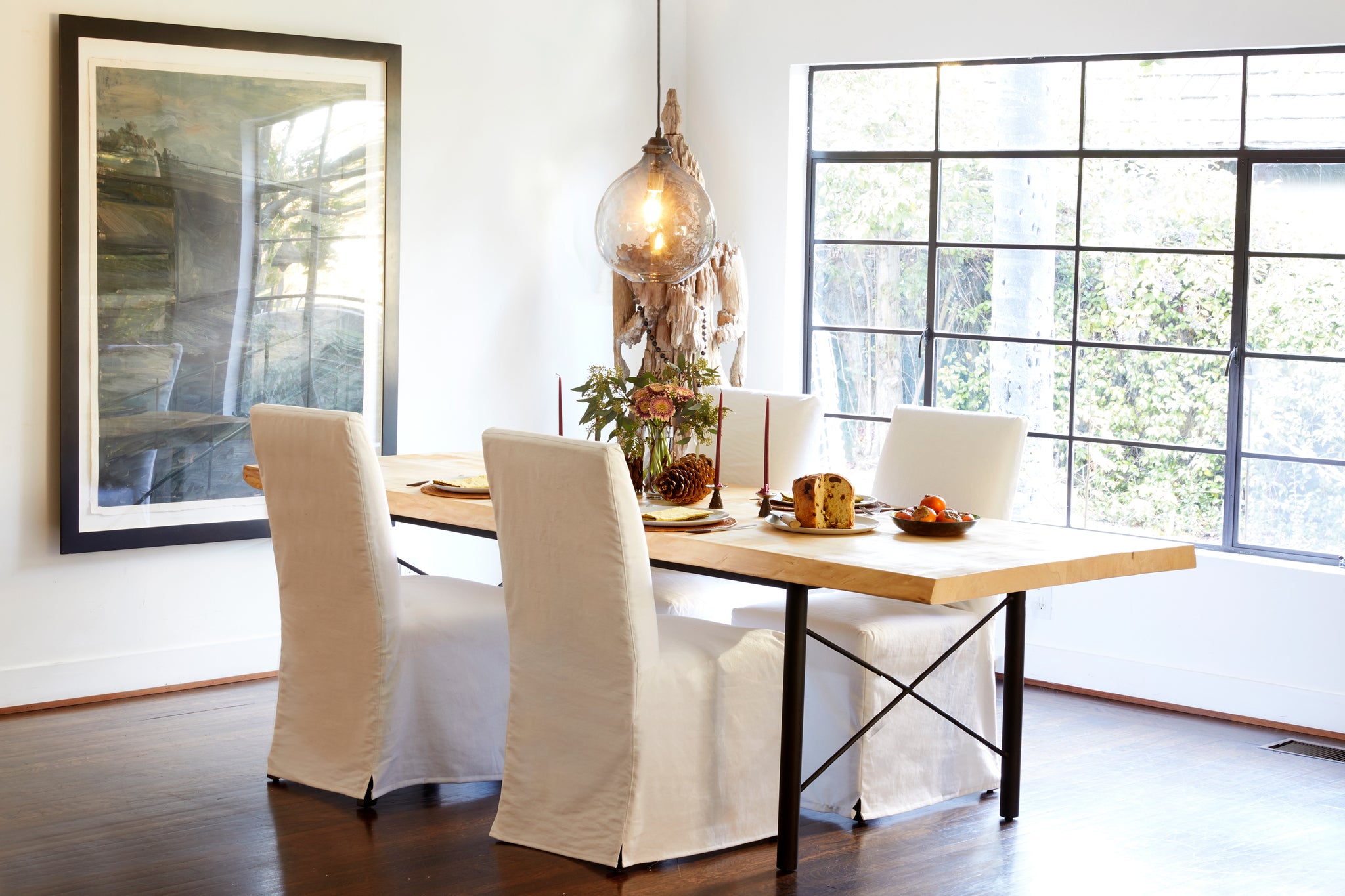  Parsons dining table in Denim White next to a wood dining table. In the background is a white room with a large picture frame and glass window. Above the chairs hangs a jug lamp. Photographed in Denim White. 