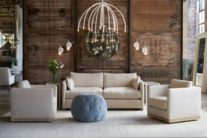  Sofa and 2 chairs in a showroom with a blue pouf in the middle and a white chandelier. Photographed in Velluto Cloud. 
