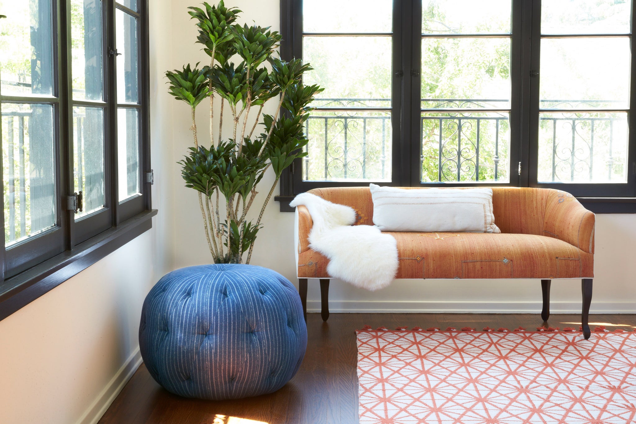  Pouf Ottoman 26 in Bengal Pin Stripe Indigo next to a tan sofa and potted plant. Photographed in Bengal Pin STripe Indigo. 