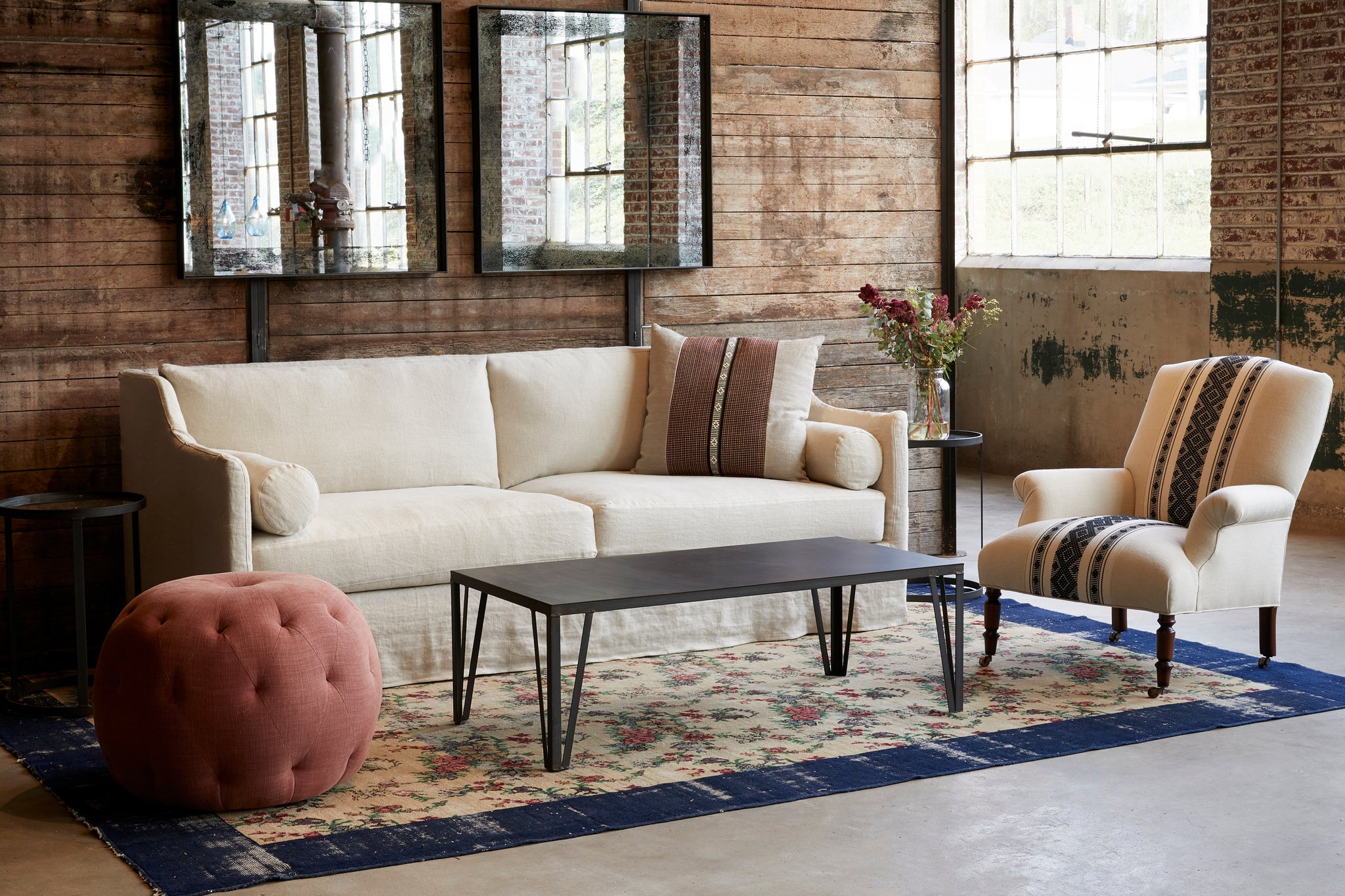  Pouf Ottoman 26 in Rye Terra next to a coffee table, a light sofa, and chair. Photographed in Rye terra. 