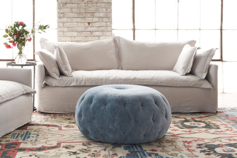 White sofa in front of window and blue velvet ottoman in front. Photographed in Velluto Cloud.