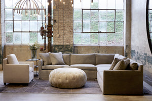  Pouf Ottoman 43 in Velluto Stone next to a tan chair and sectional. Photographed in Velluto Stone. 