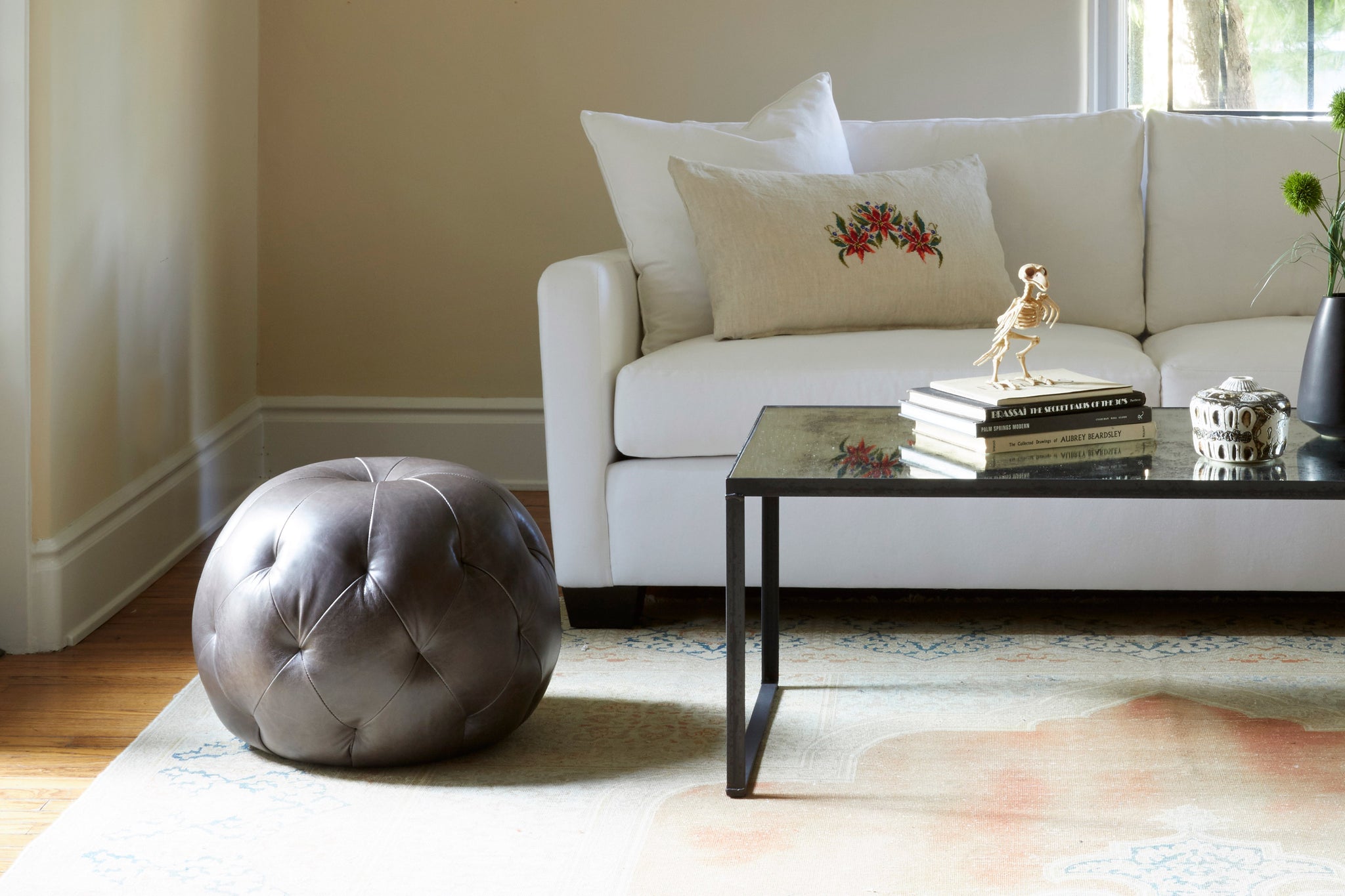  Pouf Ottoman in Indiana Charcoal next to a glass coffee table and light sofa. Photographed in Indiana Charcoal. 