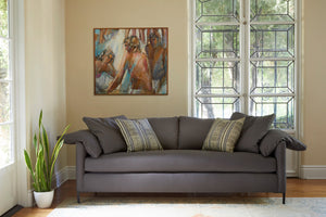  The Radley is upholstered in Logan Grey, photographed in a living room with plenty of daylight coming through a large door window behind the sofa. There are 2 decorative pillows on the sofa. A painting representing 3 people is on the back wall. There is a snake plant in a white pot on the floor, to the left of the sofa. Photographed in Logan Grey. 