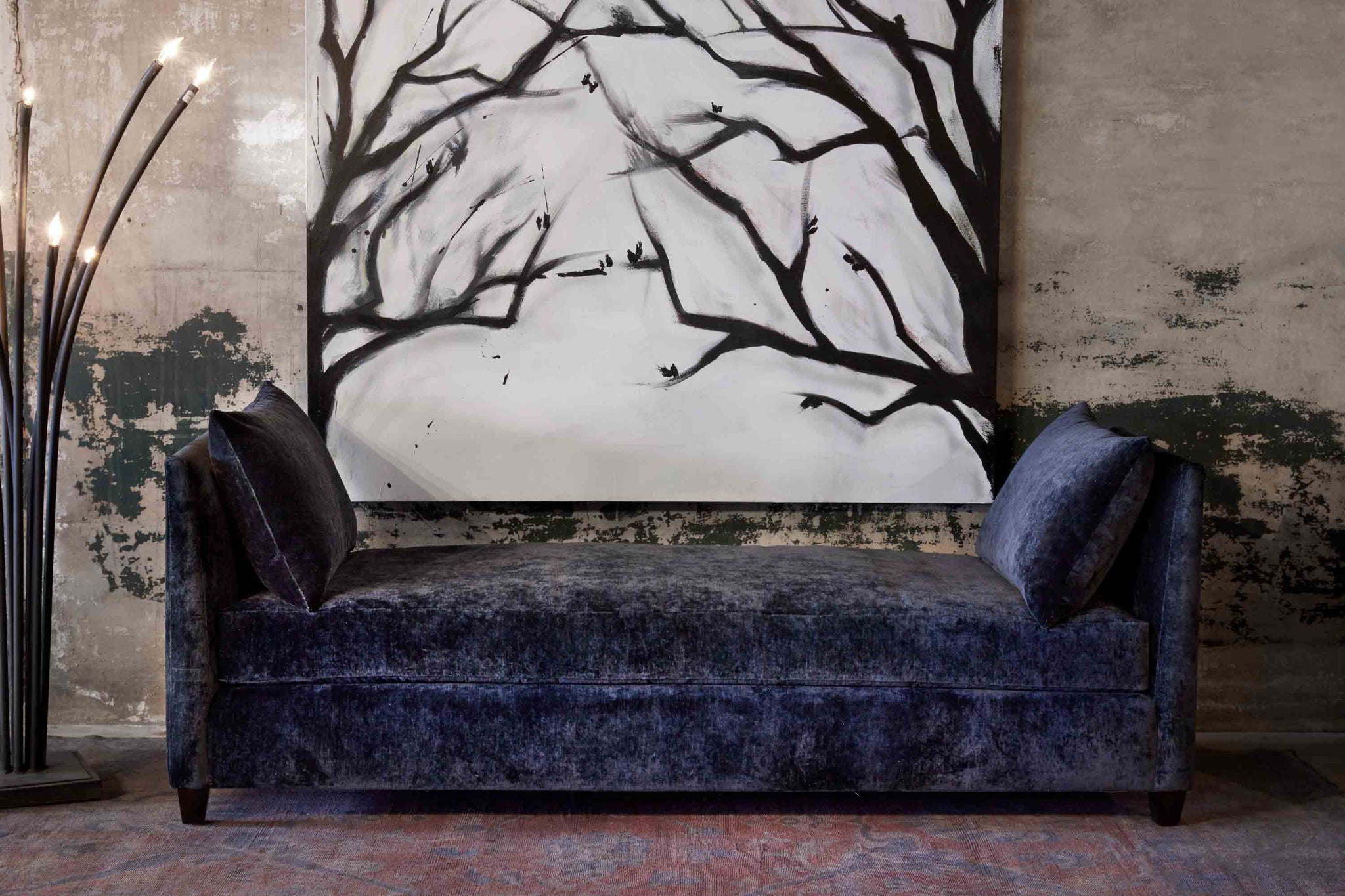  Upholstered daybed in dark blue fabric with ramo floor lamp next to it. Placed against distressed brick wall. 