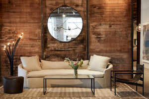  Ramo floor lamp next to upholstered sofa in light fabric against distressed wood wall.  