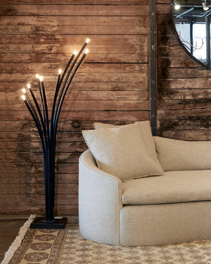  Ramo floor lamp next to upholstered sofa in light fabric against distressed wood wall. 