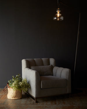  Grey chair in front of a black wall with a floor lamp on the right and a basket with flowers on the left. Photographed in Molino Ash 