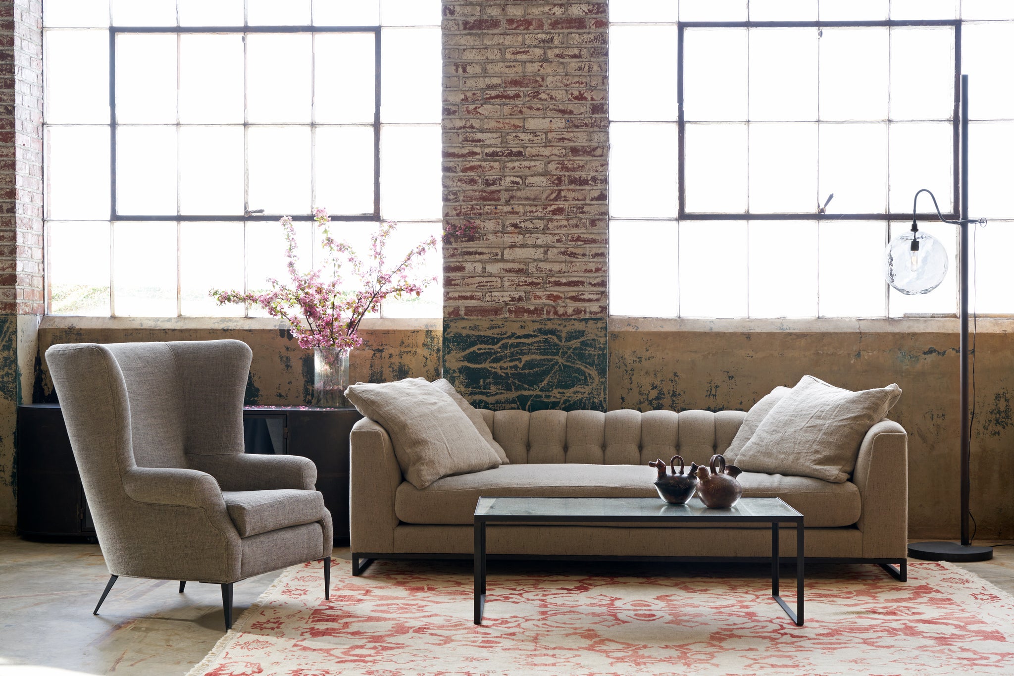  Sofa with 4 pillows in front of 2 large windows with a wing chair on the left. Photographed in Andrews Burlap. 