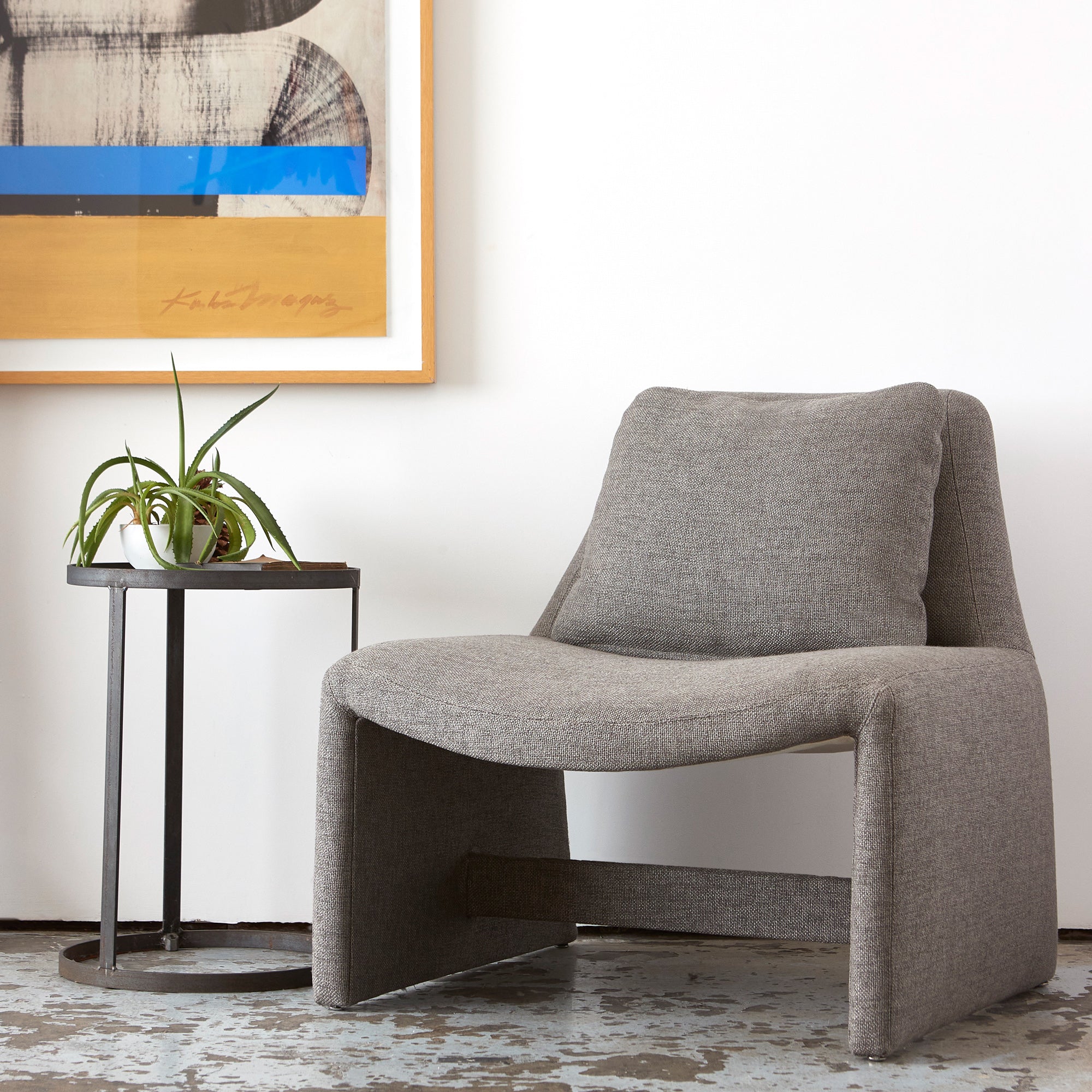  Chair in grey fabric next to a side table with a plant. 