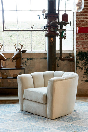 Shelby chair in Velluto Stone next to a dark table with two deer head decor. In the background is a brick wall with a large window and industrial pipe. Photographed in Velluto Stone. 