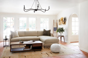  Living room with upholstered sofa in light natural fabric, rectangular wood coffee table and spider chandelier hanging above. Large Rug below sofa and pouf ottoman in white leather. 