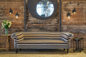  Striped sofa in front of a wood wall with a round mirror on the wall and 4 sconce lights. Photographed in Montalvo Cafe. 