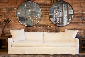  Sunset sofa slipcovered in Noah Bone in front of a wood wall with 2 round mirrors. Photographed in Noah Bone. 