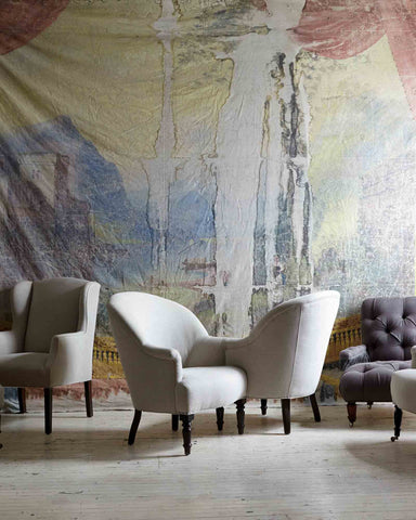 Tete-a-Tete chair in Vintage Flax next to various other chairs. In the background is a large vintage painting that takes up the entire wall. Photographed in Vintage Flax.