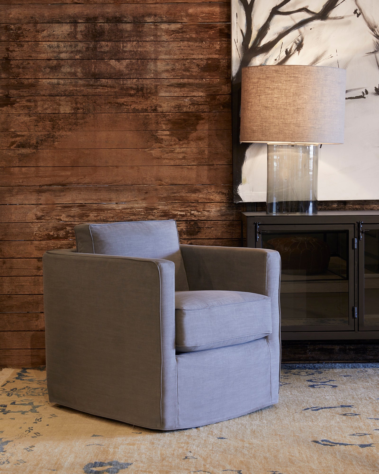  Vista Mini chair in Molino Slate next to a dark credenza. In the background is a wood wall with a painting of tree branches hanging from it. Photographed in Molino Slate. 