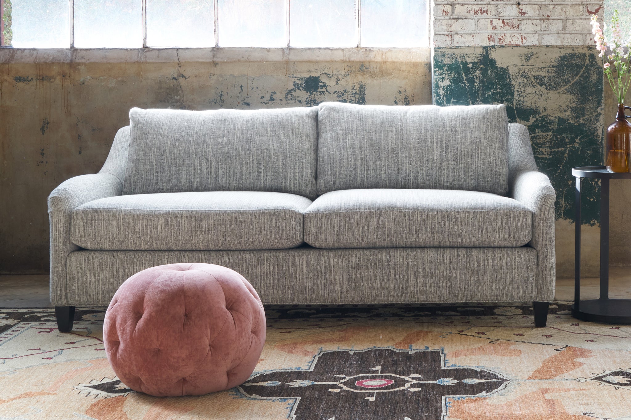  Grey Sofa with a pink velvet pouf in front. Photographed in Cameron Grey. 