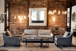  Willard chair in Molino Slate next to a metal/concrete side table. In the background is a wood wall with a lamp and white mirror hanging. Above all the pieces hangs a chandelier. Photographed in Molino Slate. 