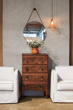  Two slip covered chairs in light fabric with tall slim dresser between. Winery wall mirror hung up above dresser and morse pendant hanging beside it.  